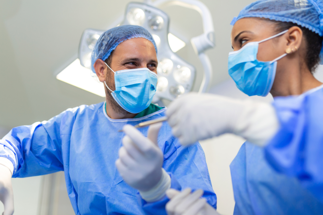 Low Angle Shot in the Operating Room, Assistant Hands out Instruments to Surgeons During Operation. Surgeons Perform Operation. Professional Medical Doctors Performing Surgery.